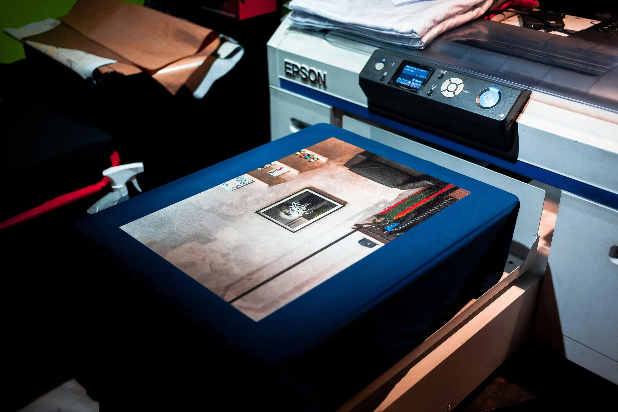 A direct-to-garment printer with a navy t-shirt stretched over the platen, a full-colour photographic print freshly laid on the chest panel.