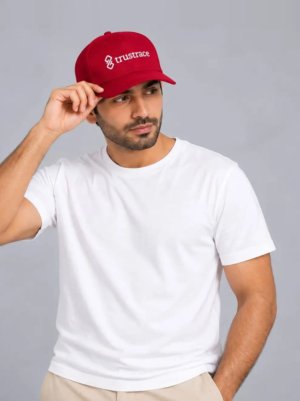 A model in a white t-shirt adjusting a red six-panel cap, the trustrace logo embroidered across the front.
